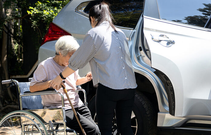 caregiver helping disabled elderly woman in wheelchair to get into the car